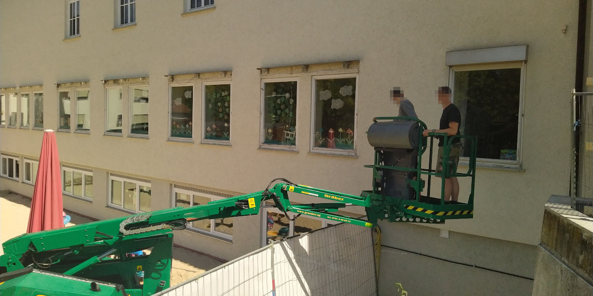 Zwei Arbeiter auf einer Hebebühne vor einem Fenster