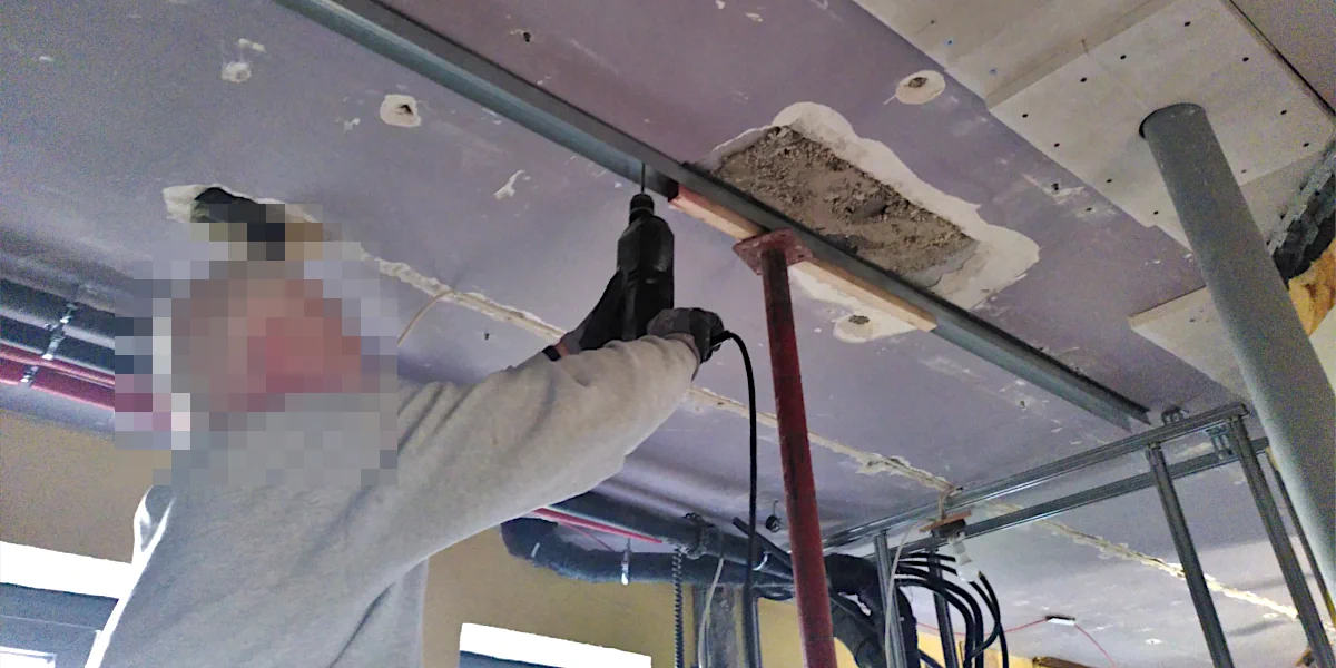 Ein Arbeiter bohrt ein Loch in die Decke um eine Aluschiene zu befestigen