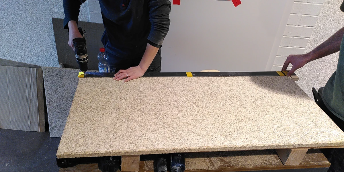 Mit einem Akkuschrauber werden Löcher in eine Sauerkrautplatte gebohrt